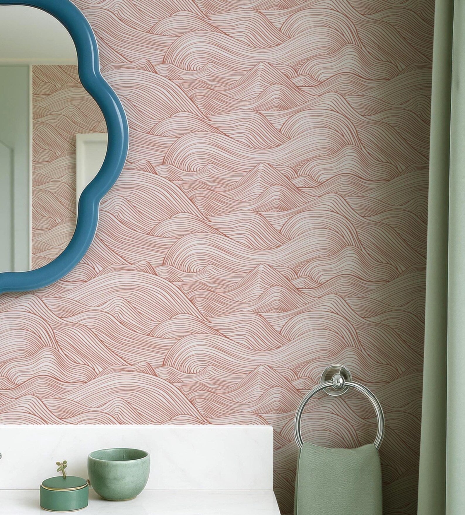 a bathroom with a pink and white wave-patterned wallpaper, a blue oval mirror, a white sink, and a green towel.