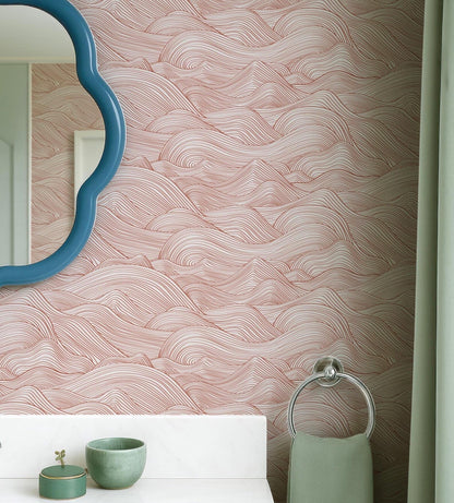 a bathroom with a pink and white wave-patterned wallpaper, a blue oval mirror, a white sink, and a green towel.