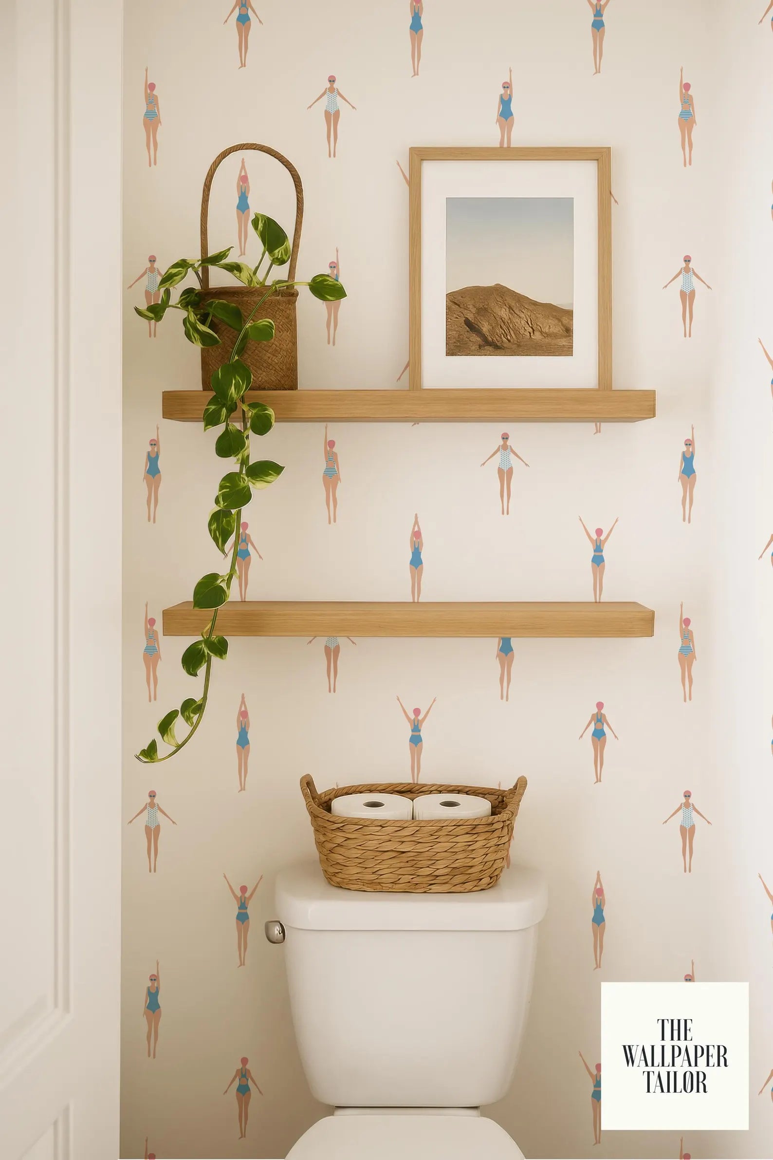 a bathroom with a toilet, a basket of toilet paper, and a framed picture on a shelf. The bathroom has a patterned wallpaper with illustrations of people in swimsuits.