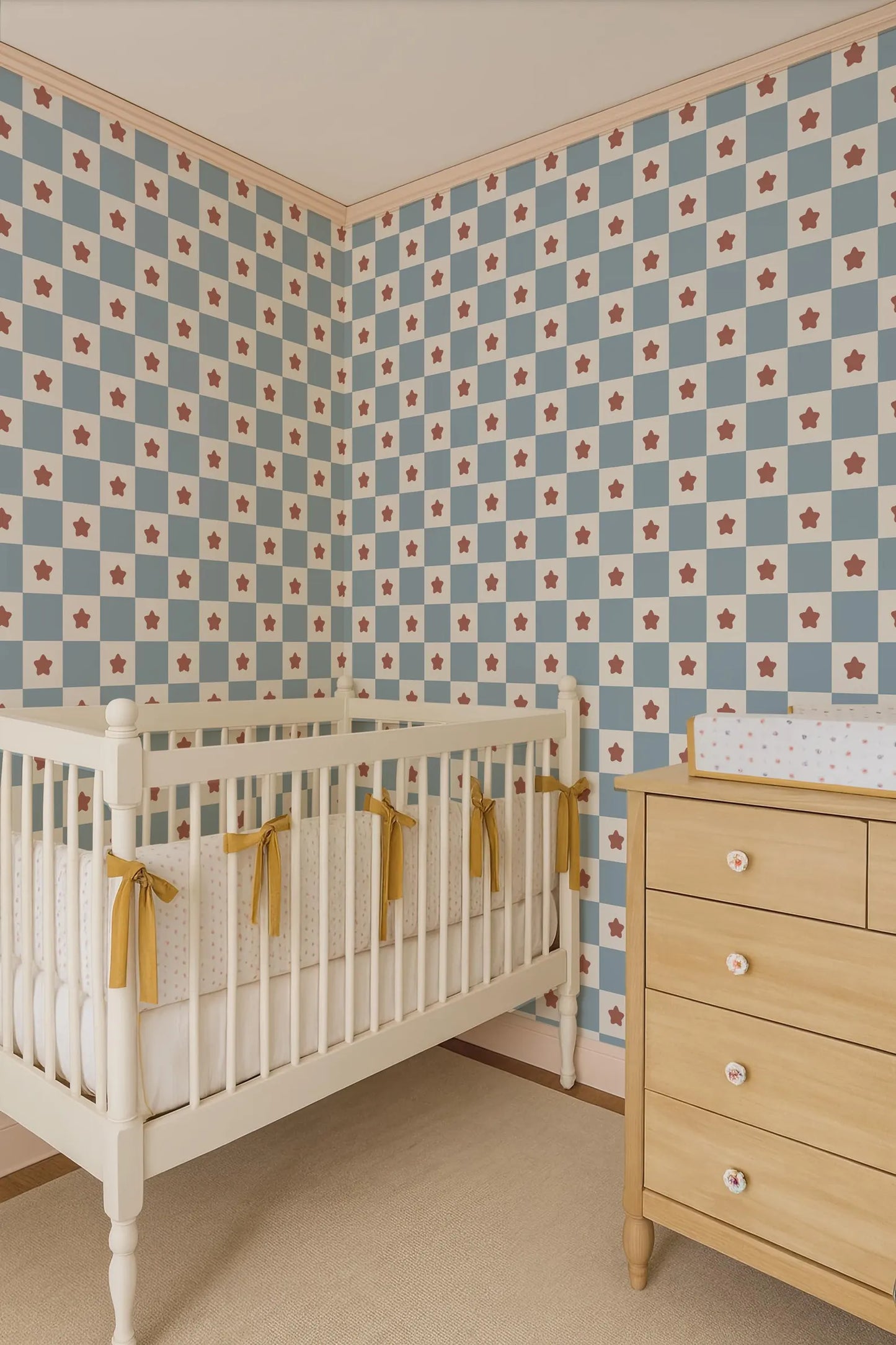 a cozy nursery room with a white crib, a wooden dresser, and a patterned wallpaper with red and white stars.