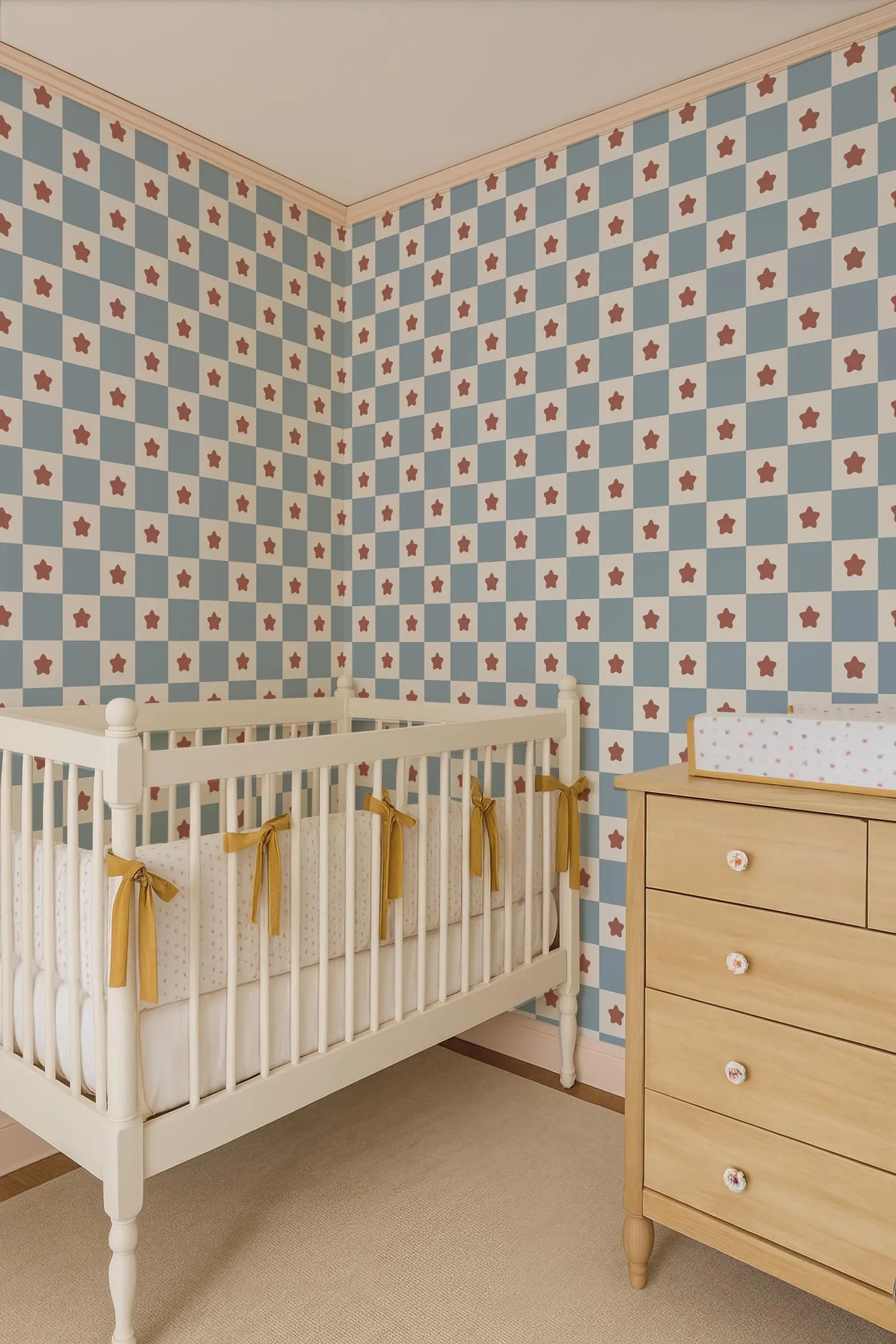 a cozy nursery room with a white crib, a wooden dresser, and a patterned wallpaper with red and white stars.