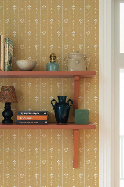 a wooden shelf with various decorative items and books, including a blue vase, a white bowl, a green vase, and a stack of books. The shelf is set against a wall with a floral wallpaper pattern.