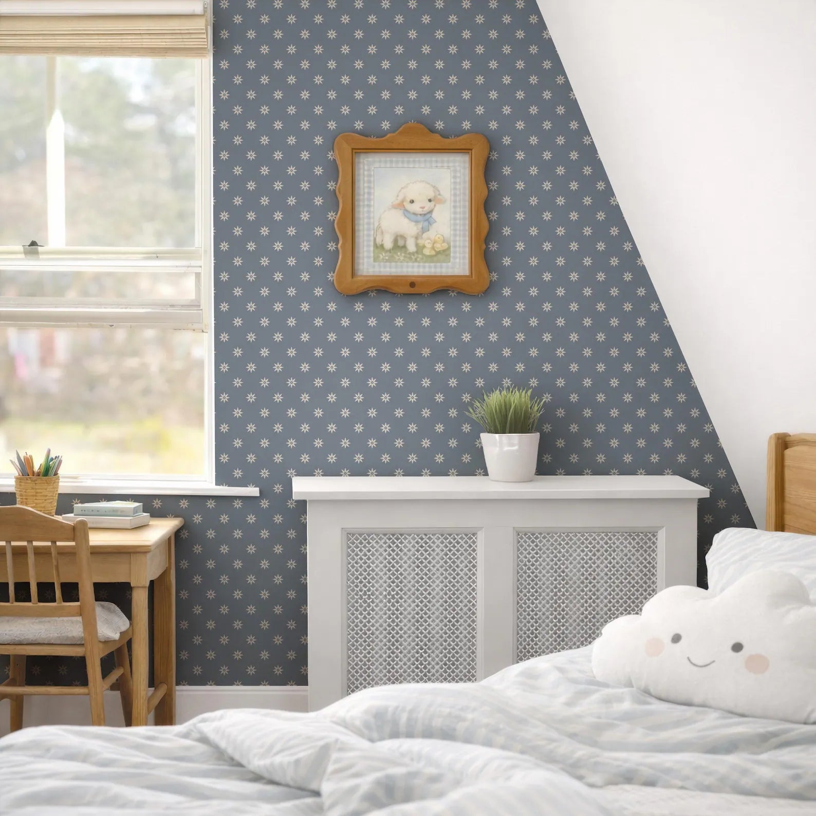 a cozy bedroom with a bed, a desk, and a window. The room has a blue and white color scheme, with a framed picture of a sheep hanging on the wall. The bed has a cloud-shaped pillow on it, and there is a potted plant on the desk. The overall atmosphere of the room is warm and inviting.