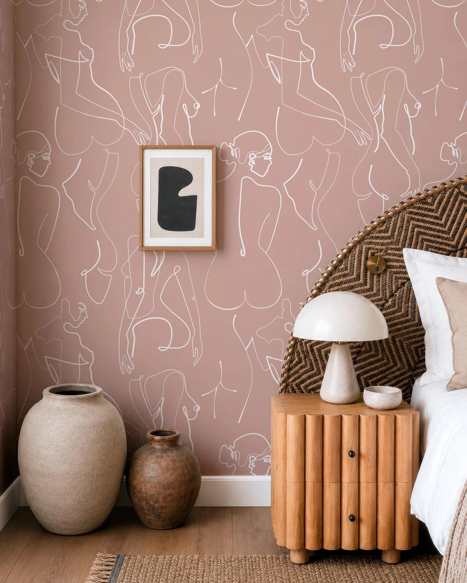 a bedroom with a pink wall, a wooden headboard, and a wooden nightstand with a lamp. There are two large vases on the floor, and a framed artwork is hanging on the wall.
