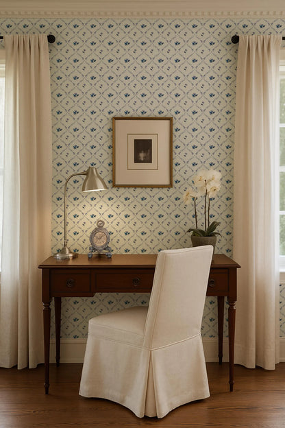 a cozy corner of a room with a wooden desk, a white chair, and a framed picture on the wall. The room has a patterned wallpaper and a window with curtains.