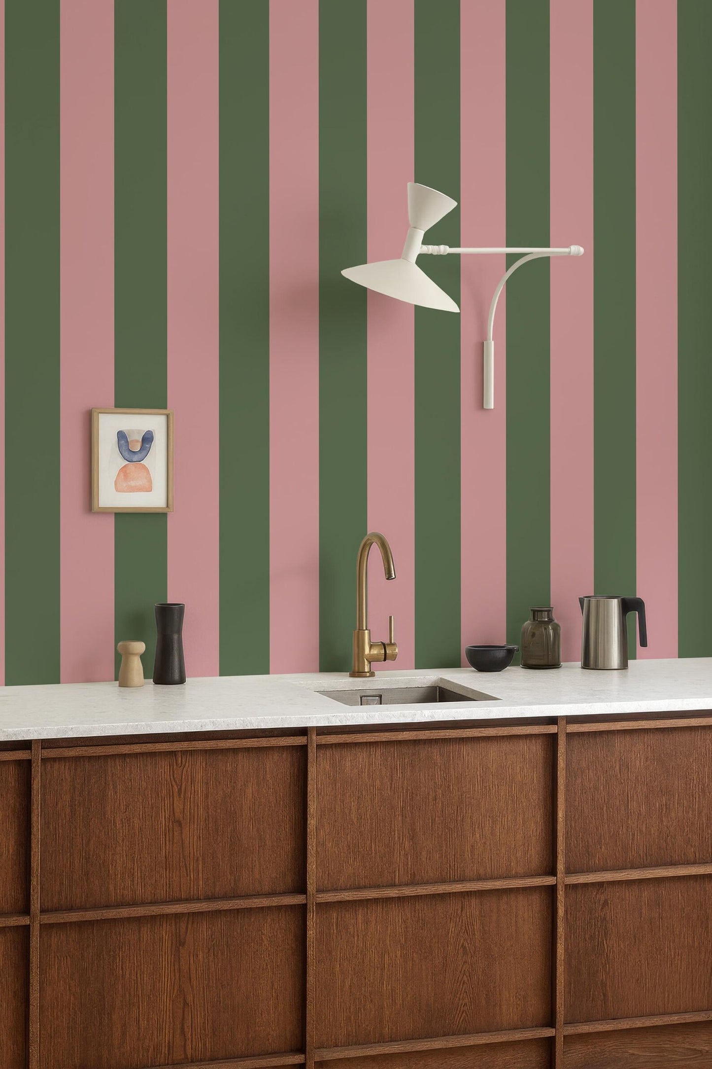 a kitchen with a white countertop, a gold faucet, and a framed picture on the wall. The kitchen has a modern and stylish design, with a striped green and pink wall behind the countertop.
