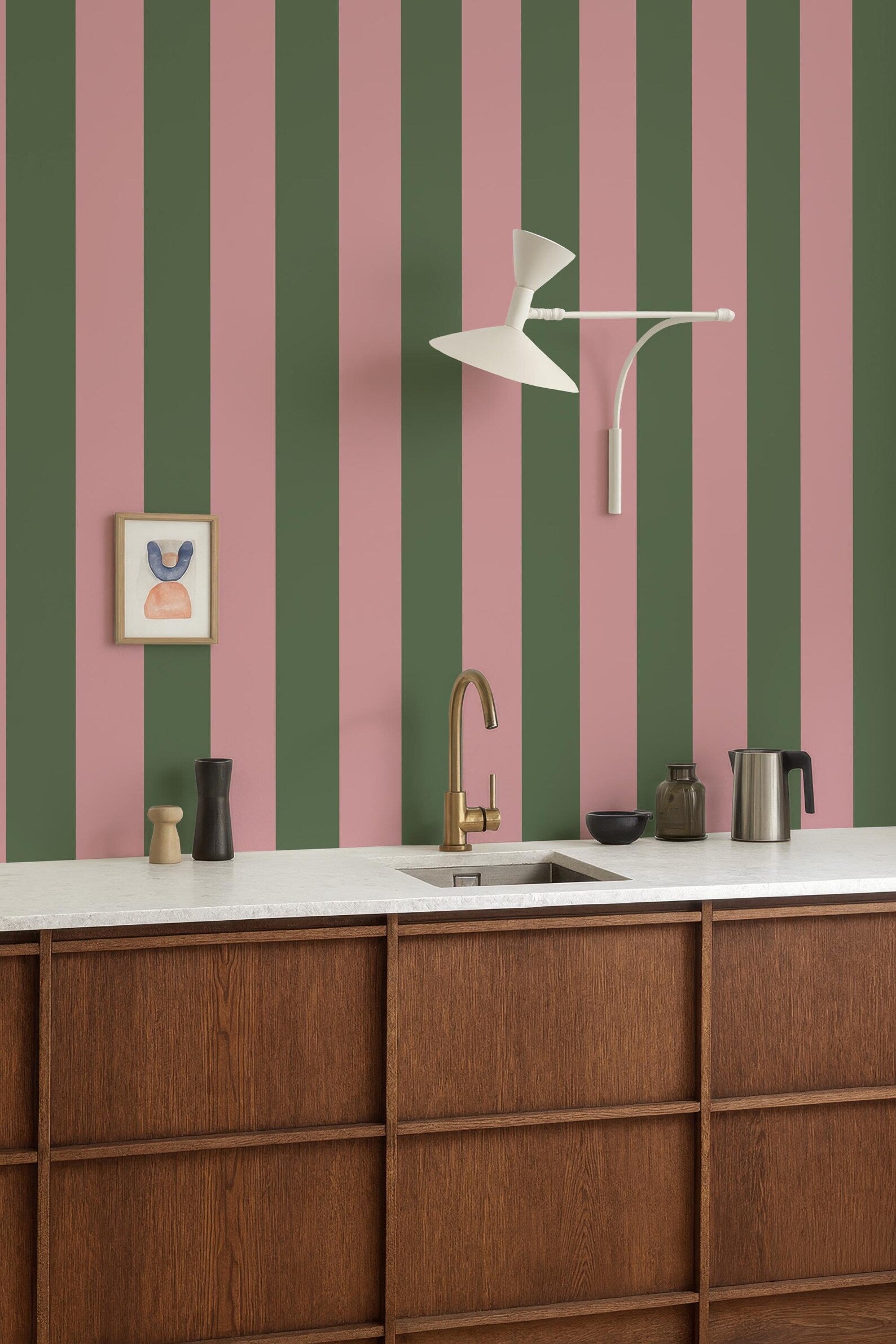 a kitchen with a white countertop, a gold faucet, and a framed picture on the wall. The kitchen has a modern and stylish design, with a striped green and pink wall behind the countertop.