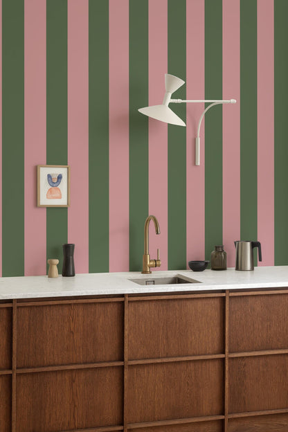 a kitchen with a white countertop, a gold faucet, and a framed picture on the wall. The kitchen has a modern and stylish design, with a striped green and pink wall behind the countertop.