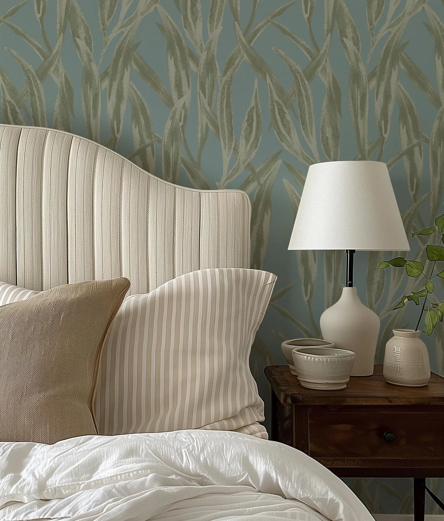 a well-organized bedroom with a bed, a nightstand, and a lamp. The bed has a white headboard and a striped pillow, and the nightstand has a lamp and a small bowl. The wall behind the bed has a patterned wallpaper, and there is a plant on the nightstand.