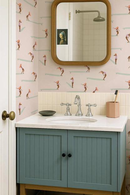 a bathroom with a blue cabinet, a white sink, and a mirror above it. The walls are decorated with a pattern of cartoon-like figures, and there is a picture of a woman in a pearl earring on the wall.