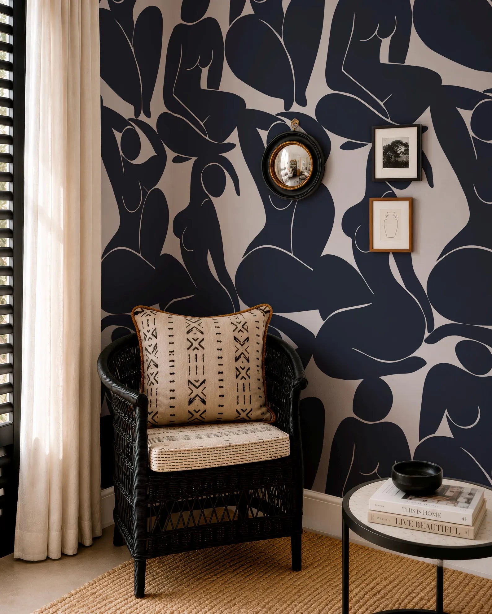 a living room with a black wicker chair, a round coffee table, and a mirror on the wall. The wall has a black and white abstract pattern, and there are framed pictures and a round mirror above the chair.