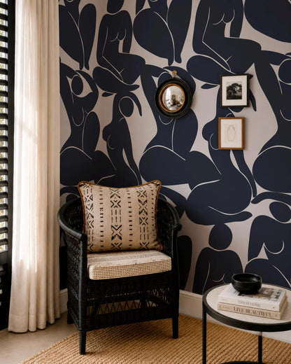 a living room with a black wicker chair, a round coffee table, and a mirror on the wall. The wall has a black and white abstract pattern, and there are framed pictures and a round mirror above the chair.