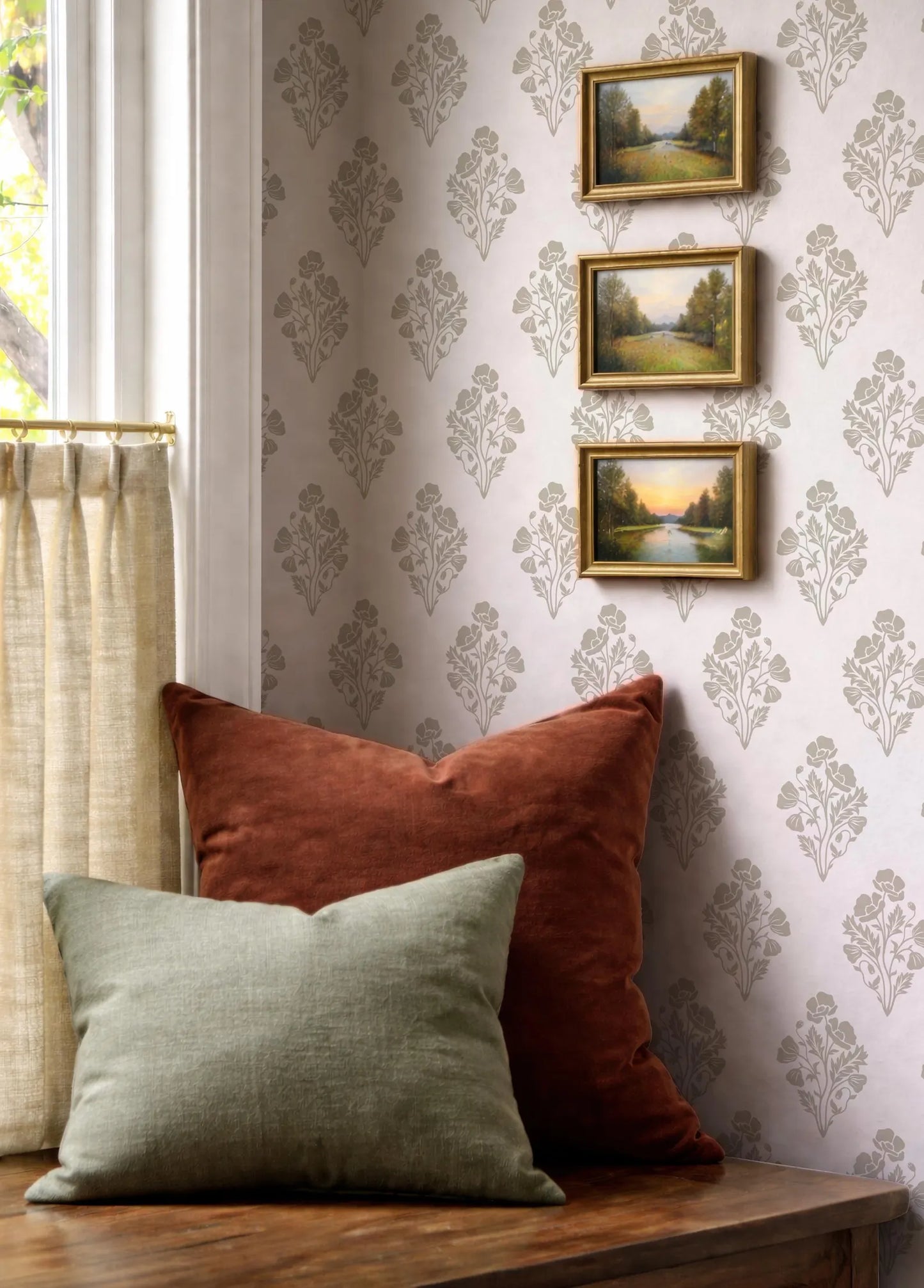 a cozy corner with a wooden table, a window with curtains, and three framed landscape paintings hanging on the wall above the table.