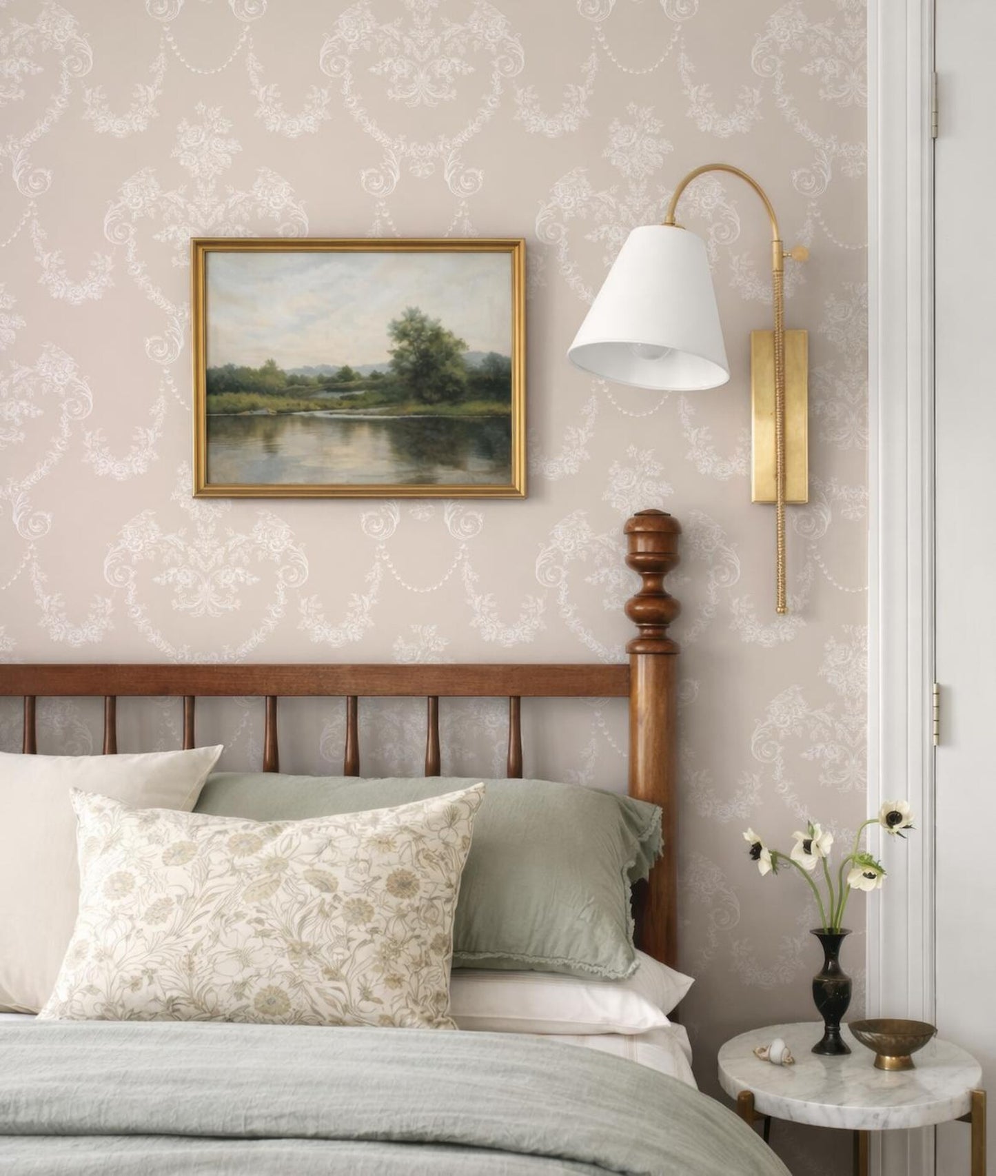 a bedroom with a wooden headboard, a framed landscape painting on the wall, and a lamp on the wall.