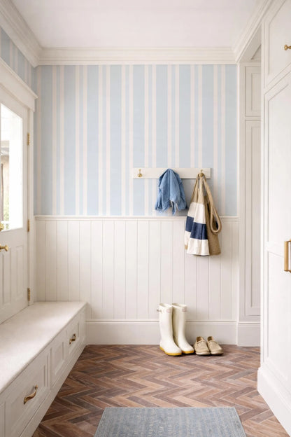 a well-organized entryway with a white bench, a coat rack with a blue and white striped towel, and a pair of white rain boots. The floor is made of wood, and the walls are painted in a light blue color with white stripes.