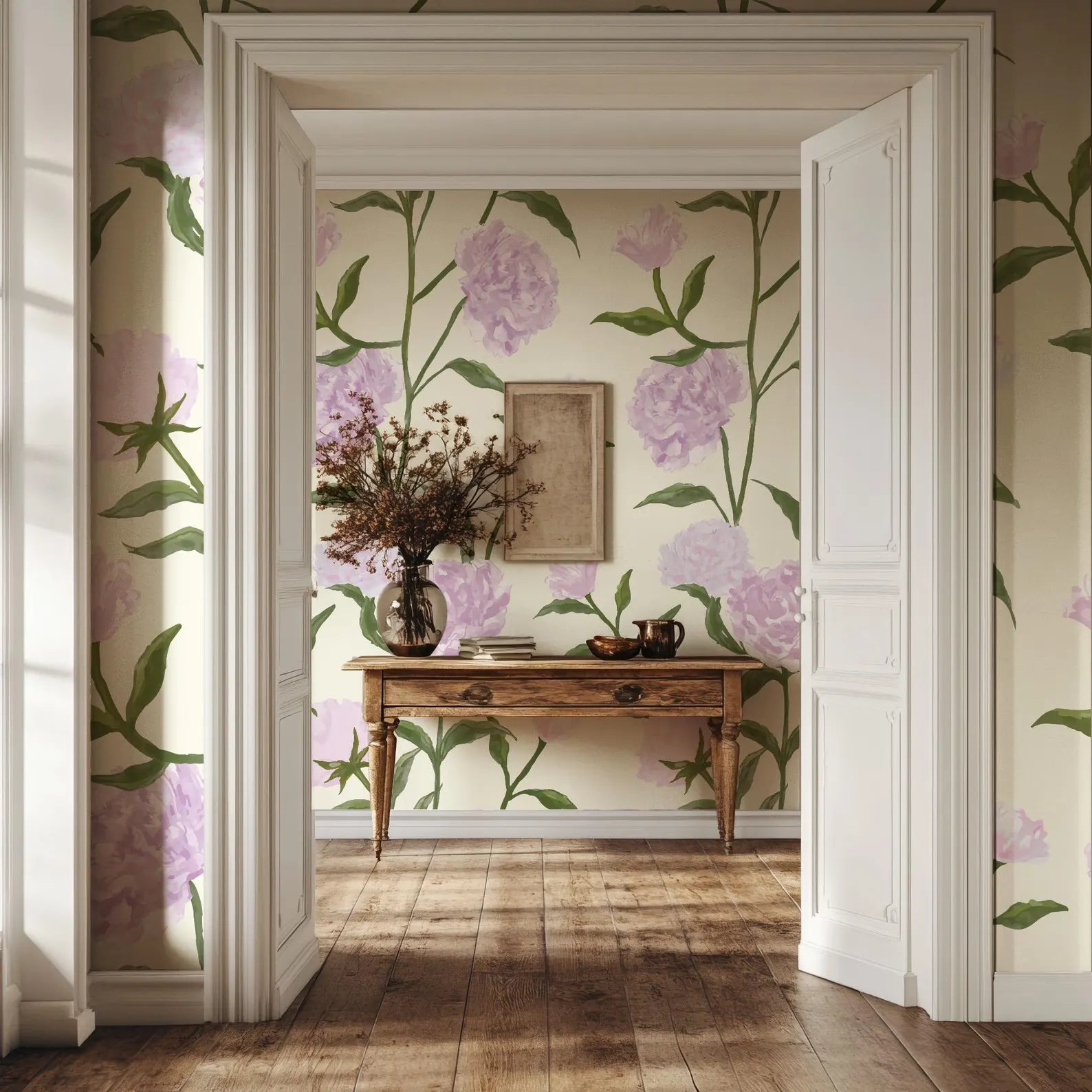a room with a wooden table, a vase of flowers, and a framed picture on the wall. The room has a floral wallpaper with pink flowers and green leaves, and the wooden floor adds a warm and natural touch to the space.