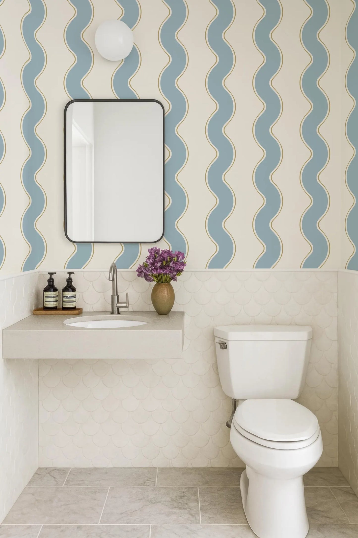 a bathroom with a white toilet, a sink with a mirror above it, and a vase of purple flowers on the counter. The walls are covered in a patterned wallpaper with blue and white stripes.