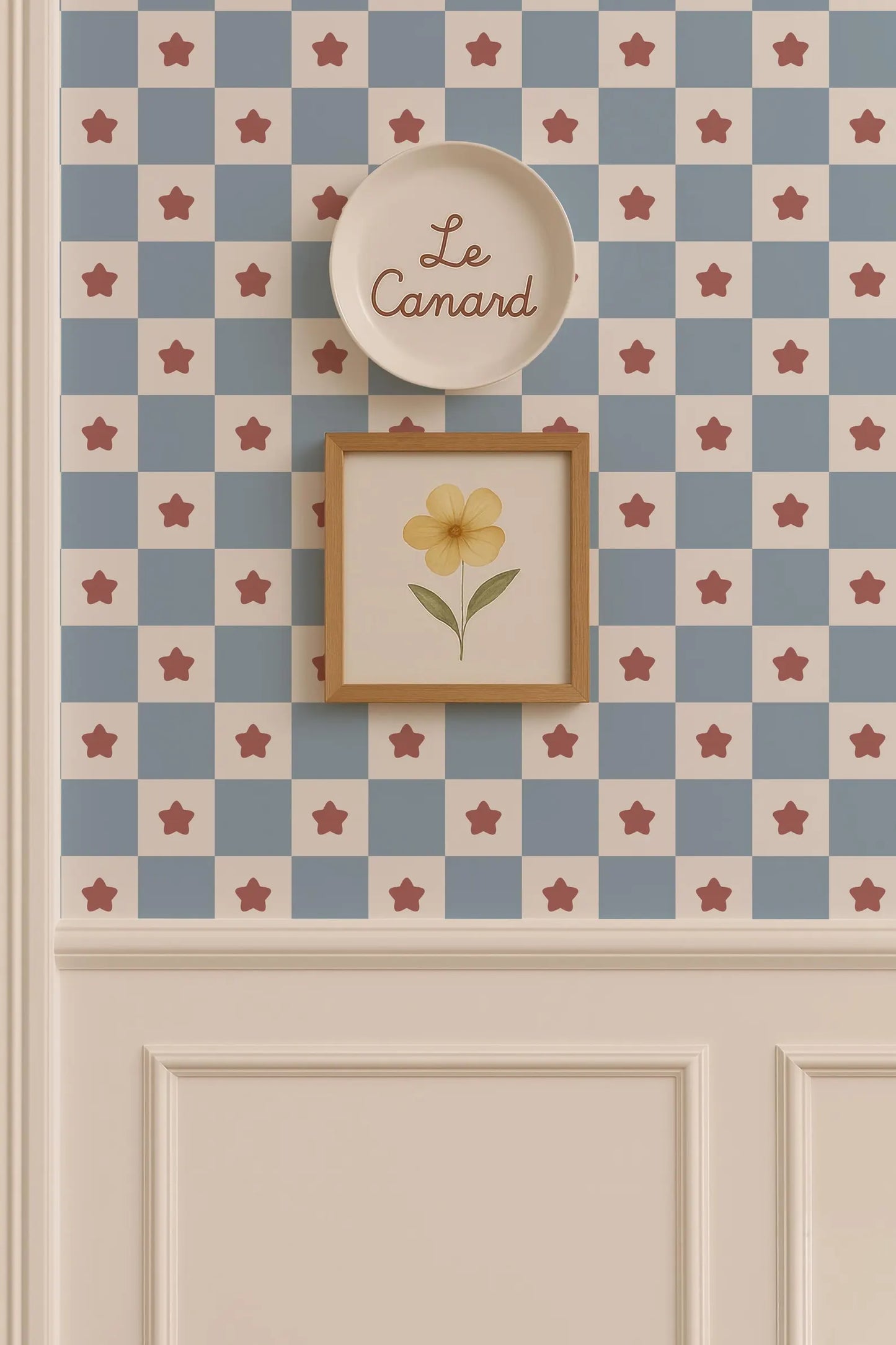 a wall with a checkered pattern in shades of blue and white, and a framed picture of a yellow flower above it. The wall also has a plate with the word "Le Camand" written on it.
