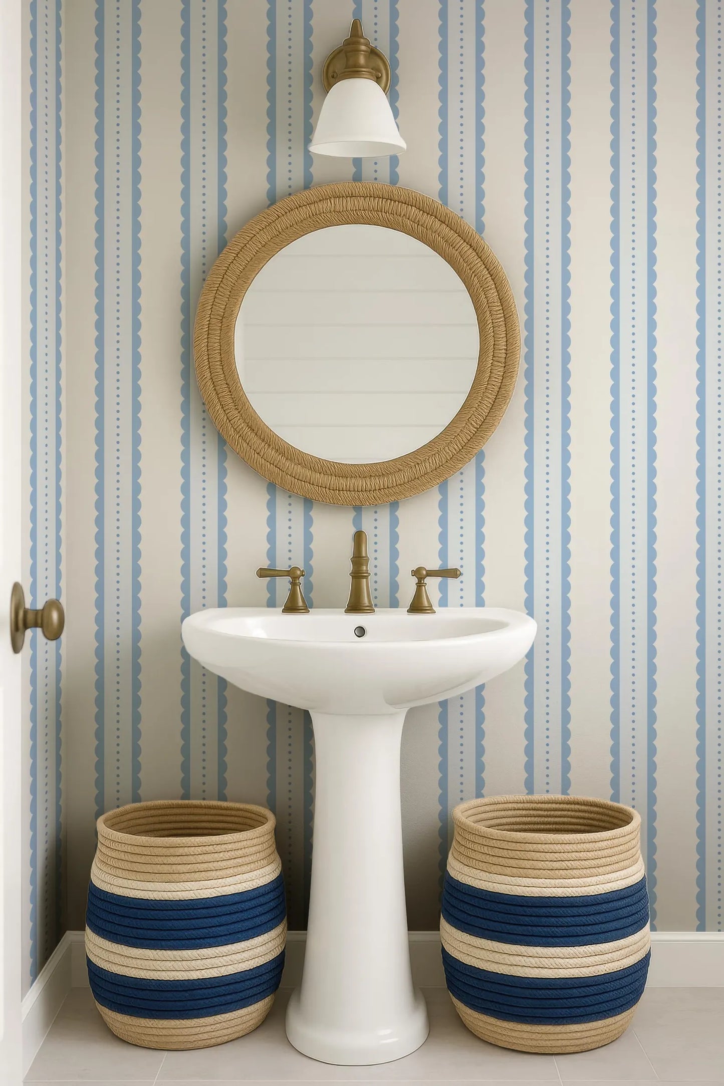 a bathroom with a white pedestal sink, a round mirror, and two woven baskets placed on the floor next to the sink.
