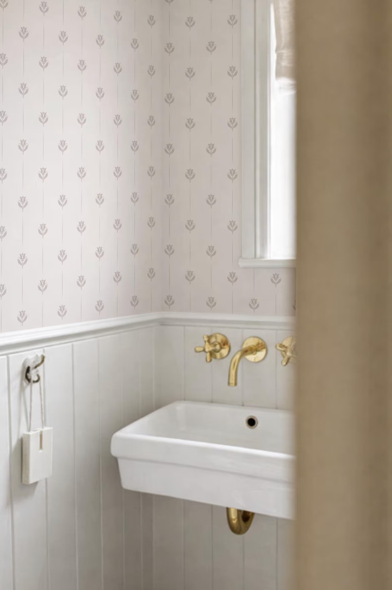 a bathroom with a white sink and gold faucets, set against a patterned wallpaper.