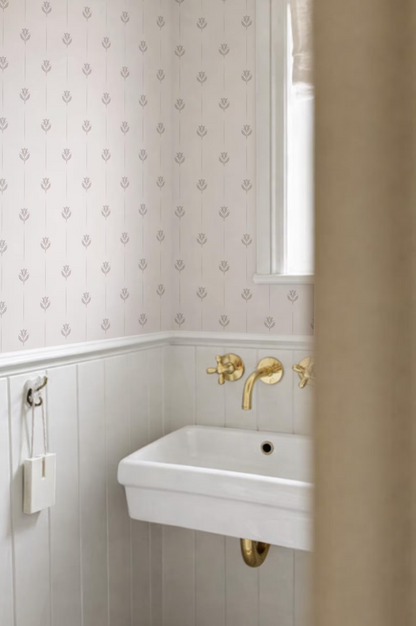 a bathroom with a white sink and gold faucets, set against a patterned wallpaper.