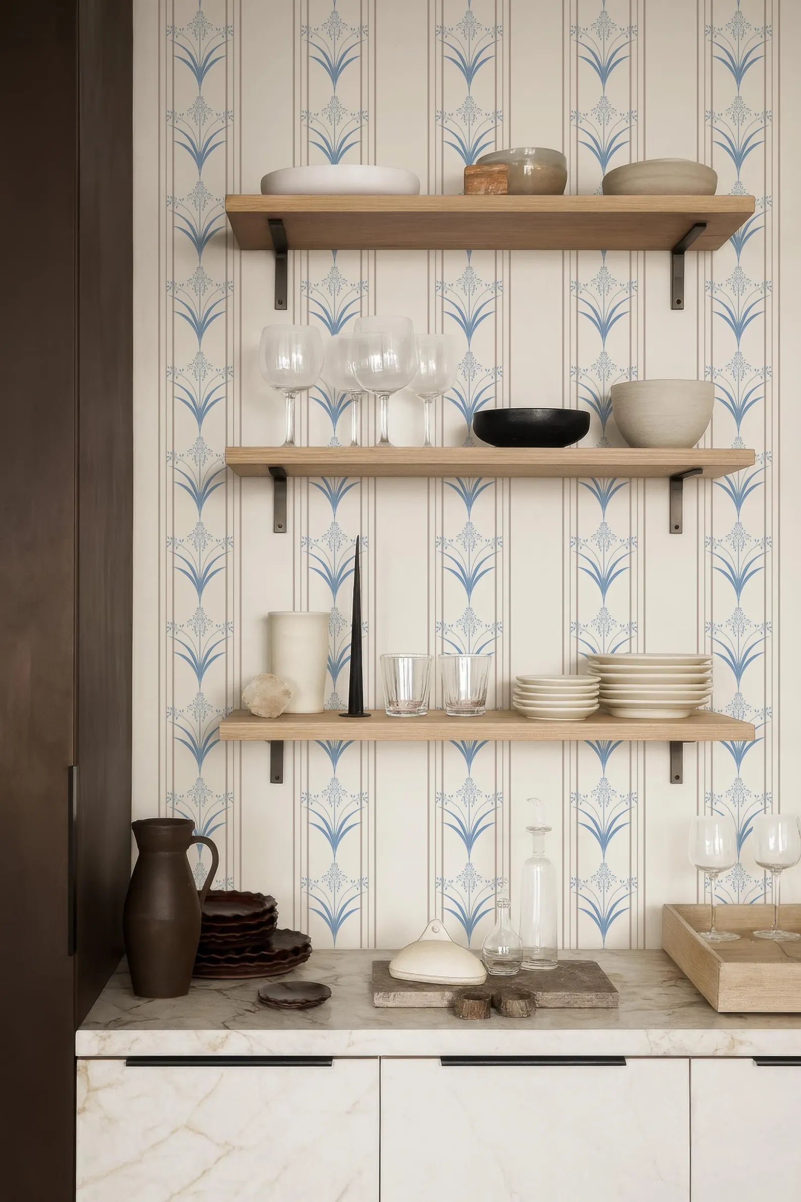 a kitchen counter with three shelves, each holding various kitchen items such as plates, bowls, and glasses. The shelves are made of wood and have a white and blue patterned design. The counter also has a marble top, and there are some decorative items like a vase and a stack of plates on it.
