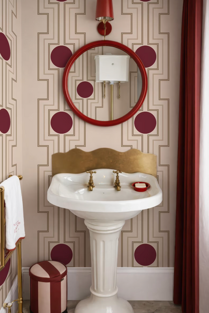 a bathroom with a white pedestal sink, a red and gold circular mirror, and a red and gold circular pattern on the walls.