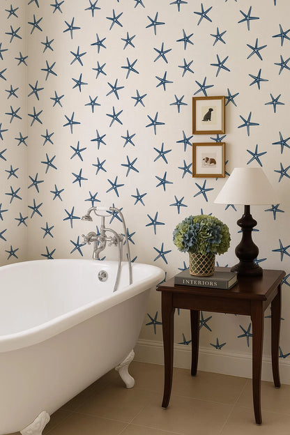 a bathroom with a white clawfoot bathtub, a wooden side table with a lamp, and a framed picture on the wall. The walls are decorated with blue star patterns, and there is a plant on the side table.