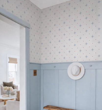 a room with a blue wall and a white hat hanging on the wall. The wall has a pattern of small stars and dots. The room appears to be a living room or a hallway, with a couch and a chair visible in the background.