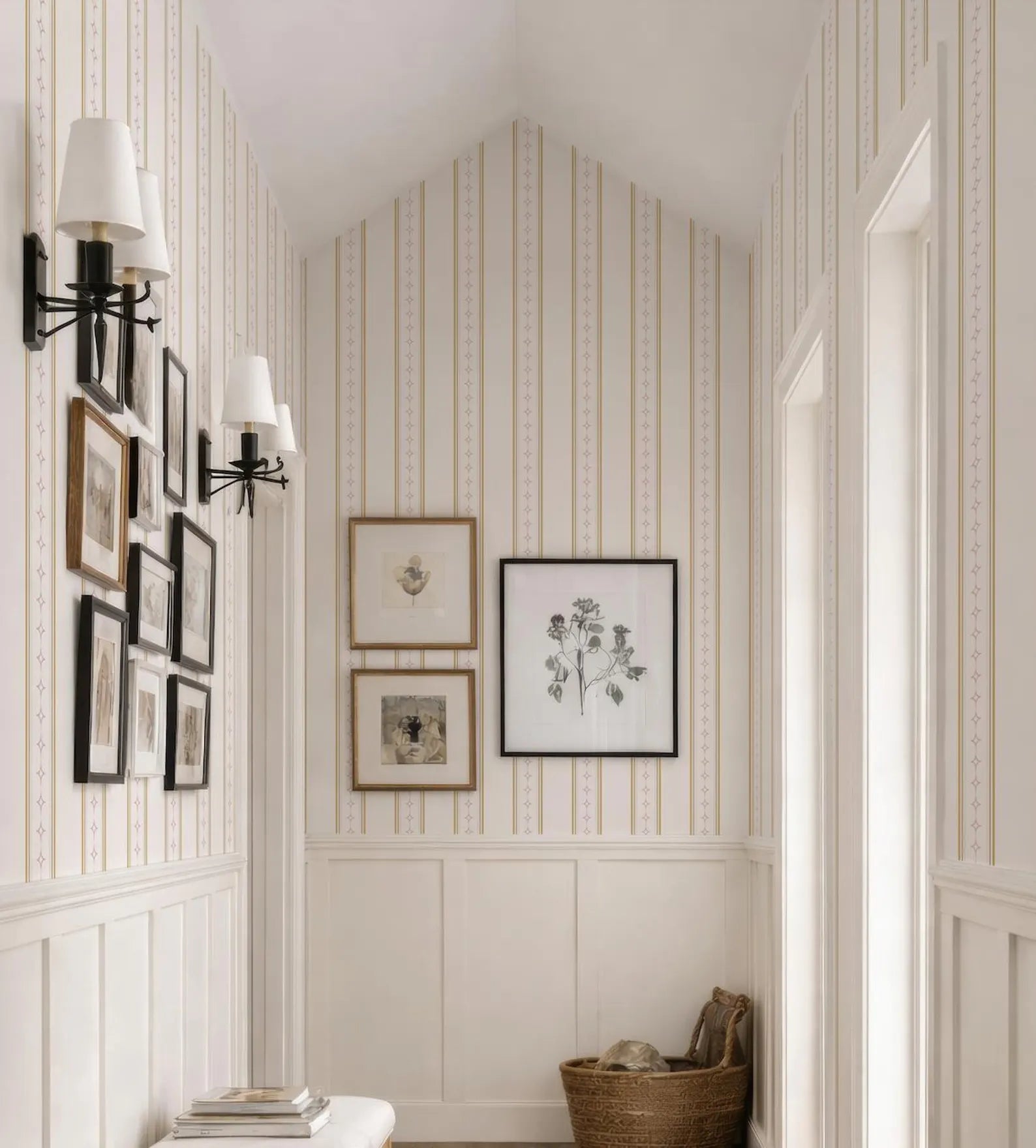 a hallway with a white and beige color scheme, featuring a ceiling with a pointed arch, a wall with framed artwork, and a basket on the floor.