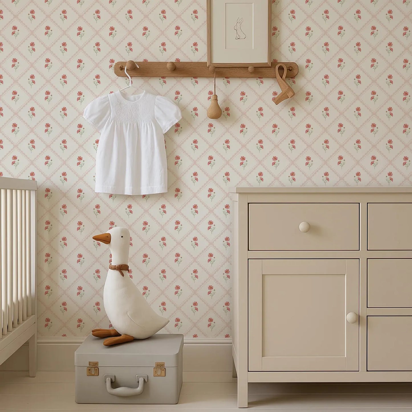 a nursery room with a white dresser, a wooden shelf with a picture frame, and a stuffed duck on a suitcase. The room has a floral wallpaper pattern.