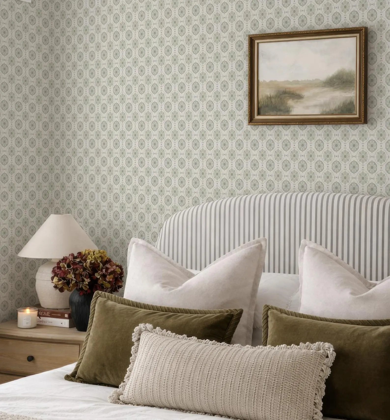 a cozy bedroom with a striped headboard, a framed landscape painting on the wall, and a bed with a white and green striped comforter and pillows.