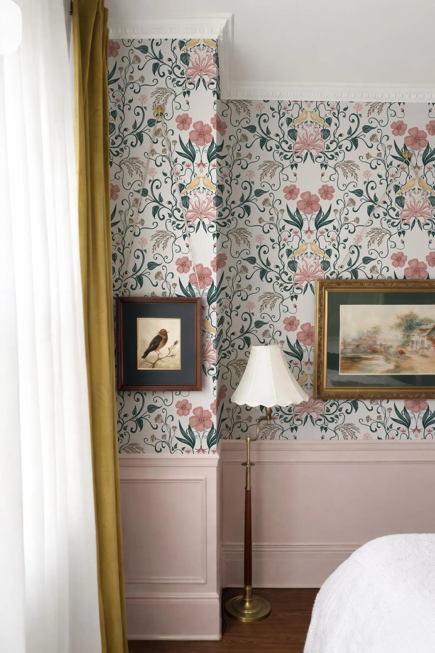 a bedroom with a floral wallpaper, a lamp, and two framed pictures on the wall.