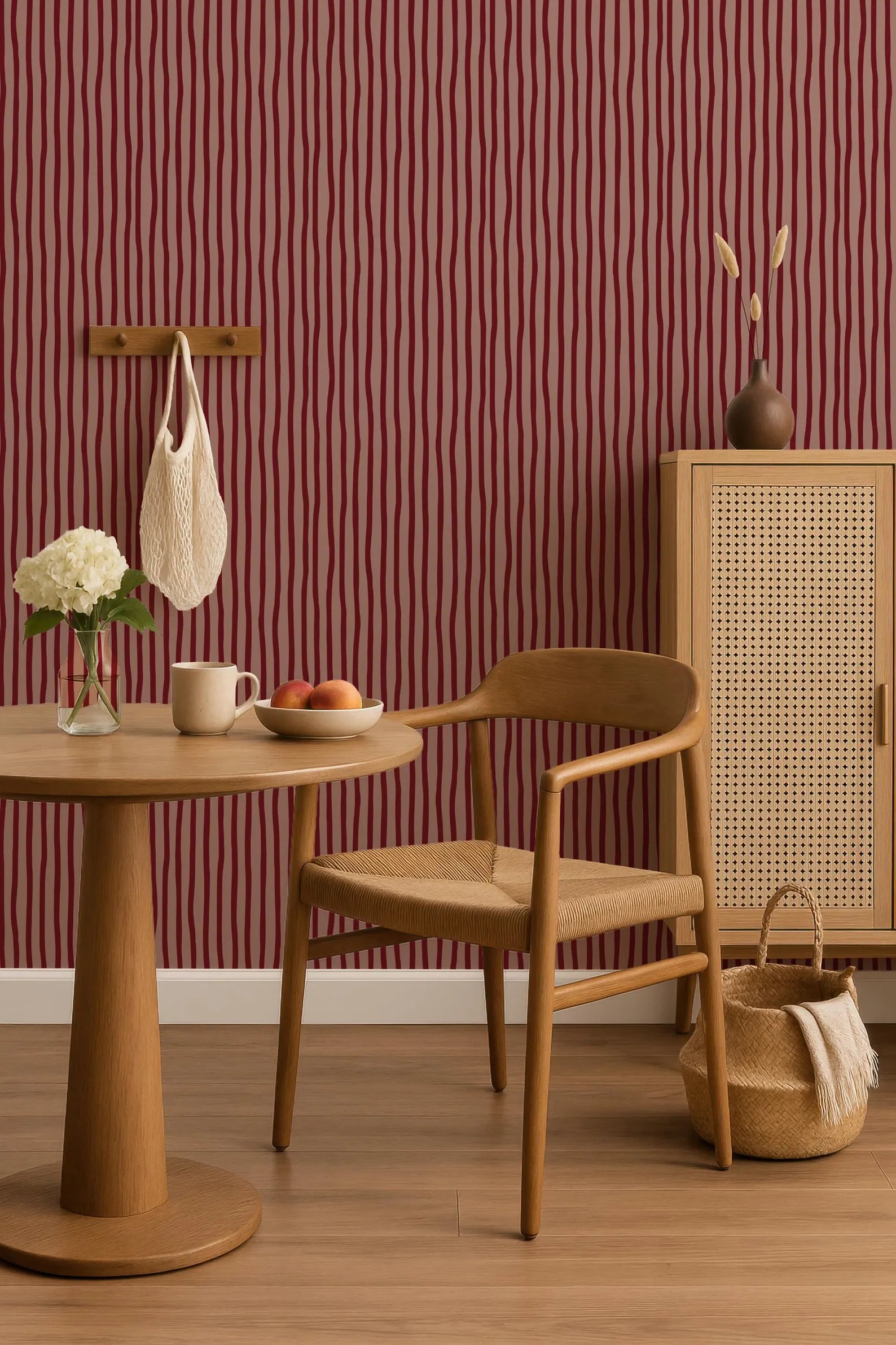 a cozy and inviting living space with a wooden chair, a round wooden table, and a woven basket. The room has a warm and rustic atmosphere, with a red and white striped wallpaper adding a touch of color. The table is set with a vase of flowers, a bowl of fruit, and a cup, creating a welcoming and comfortable environment.