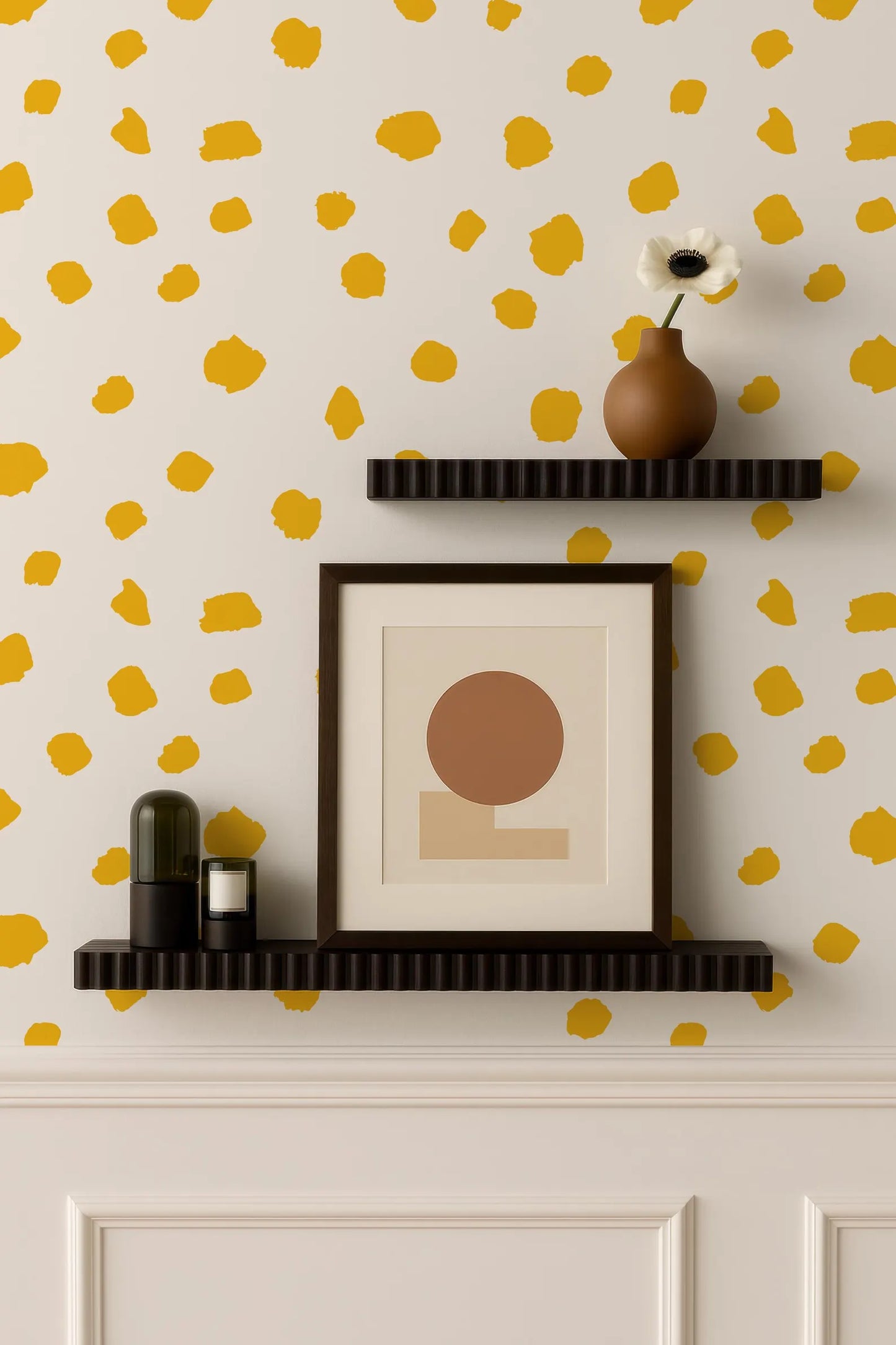 a wall with a yellow and white polka dot pattern, and two black shelves mounted on the wall. On the top shelf, there is a brown vase with a white flower, and on the bottom shelf, there is a framed picture with a brown circle in the center.