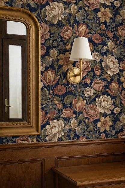 a room with a floral wallpaper, a gold-framed mirror, and a wall-mounted lamp.