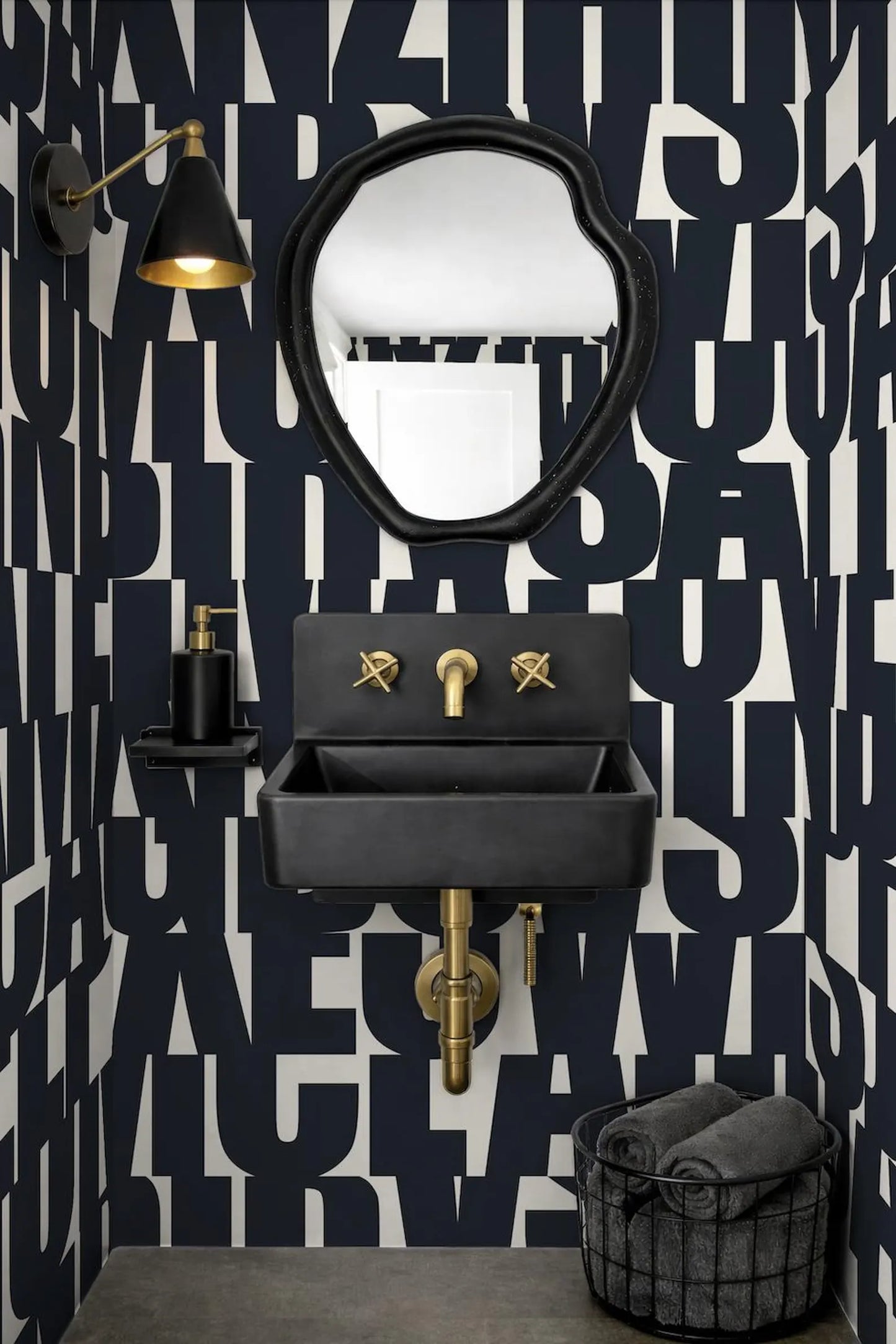 a bathroom with a black sink, a gold faucet, and a black mirror above it. The walls are covered in a black and white pattern, and there is a black basket on the floor next to the sink.