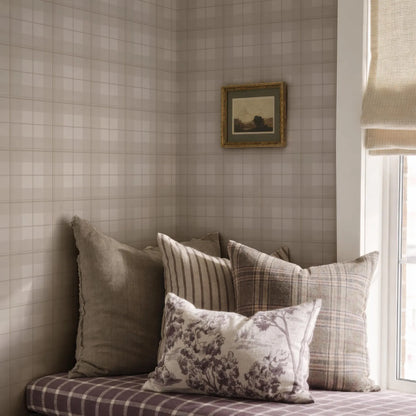 a cozy corner of a room with a plaid patterned couch, a framed landscape painting on the wall, and a window with a beige curtain.