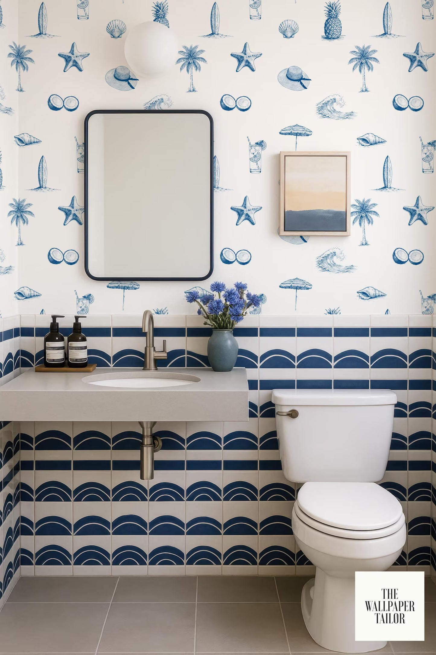 a bathroom with a blue and white tropical wallpaper pattern, a white sink, a white toilet, and a framed picture on the wall.