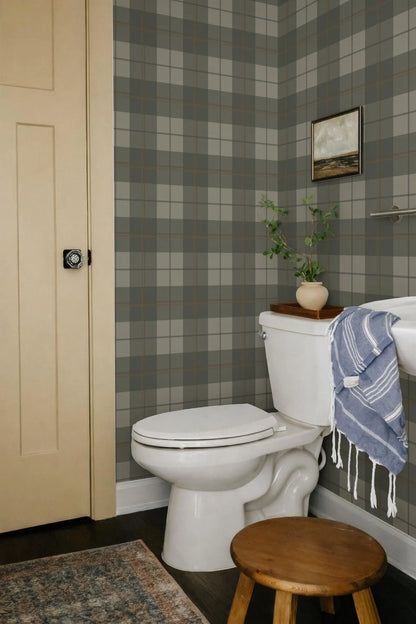 a bathroom with a white toilet, a wooden stool, and a blue and white striped towel hanging on a rack. The walls are covered in a checkered pattern, and there is a painting hanging above the toilet.