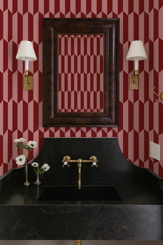 a bathroom with a black marble sink, a gold faucet, and a framed mirror above it. The walls are decorated with a red and white striped pattern, and there are two white lamps on either side of the mirror.