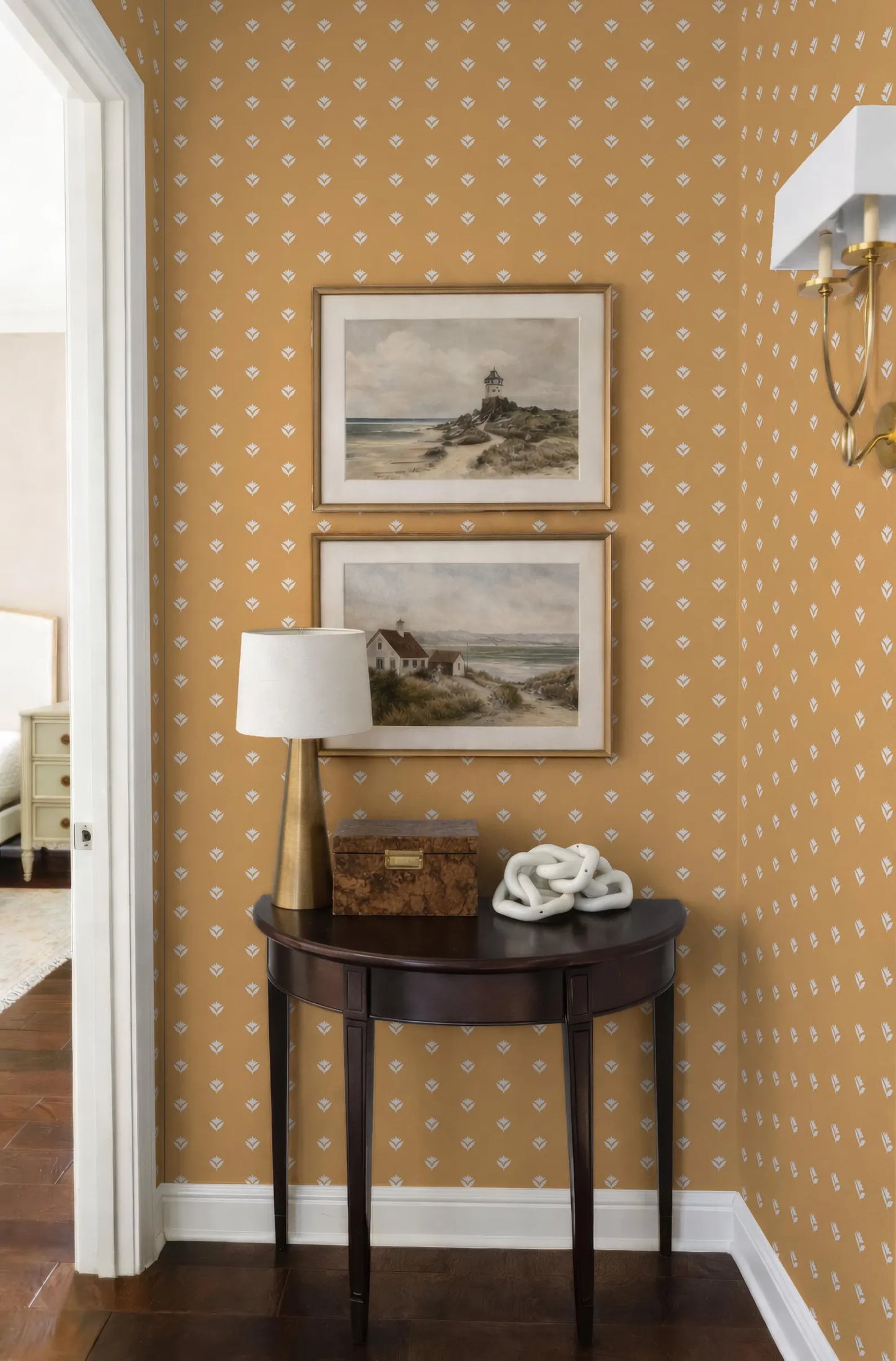 a cozy corner of a room with a wooden table, a lamp, and two framed pictures on the wall. The wall has a patterned wallpaper with a yellow and white color scheme.