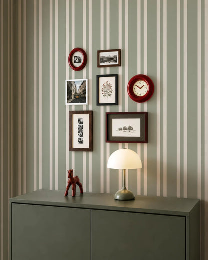 a wall adorned with a collection of framed pictures and a red clock, creating a visually appealing and decorative display.