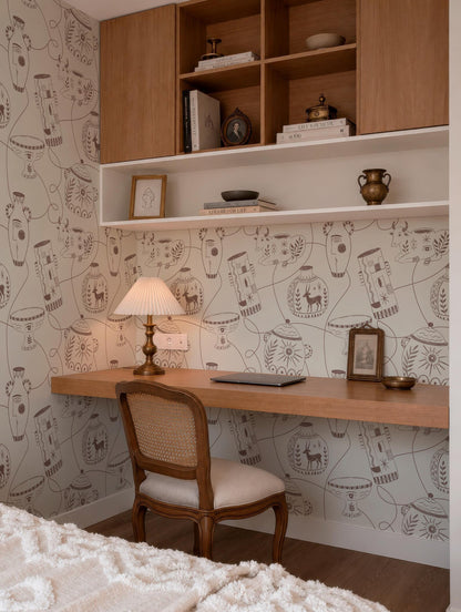 a cozy and well-organized home office space with a wooden desk, a comfortable chair, and a bookshelf above it. The wall behind the desk is adorned with a patterned wallpaper, and the room has a warm and inviting atmosphere.