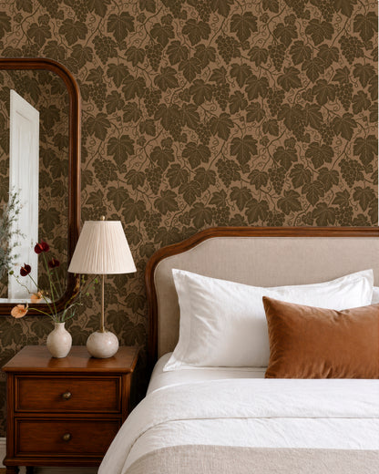 a bedroom with a bed, a nightstand, and a mirror. The wall behind the bed has a patterned wallpaper with leaves and grapes. The room has a warm and cozy atmosphere, with a brown and white color scheme.