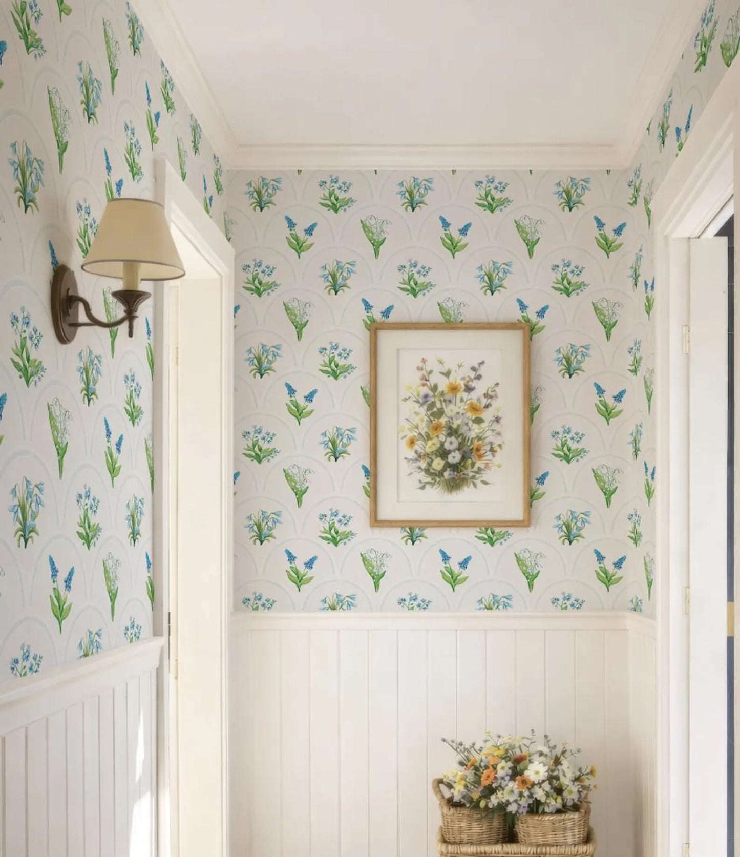 a hallway with a floral wallpaper pattern, a framed picture of flowers on the wall, and a wicker basket filled with flowers on the floor.