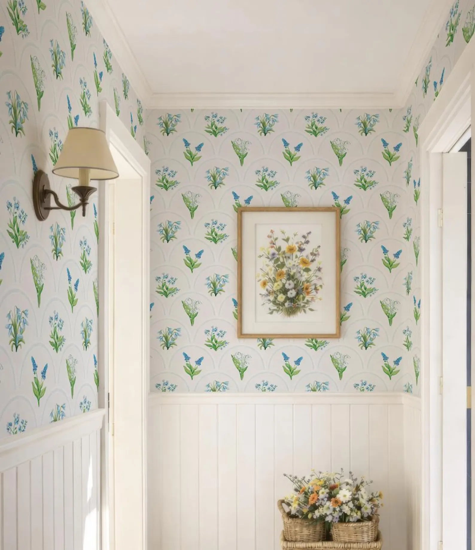 a hallway with a floral wallpaper pattern, a framed picture of flowers on the wall, and a wicker basket filled with flowers on the floor.