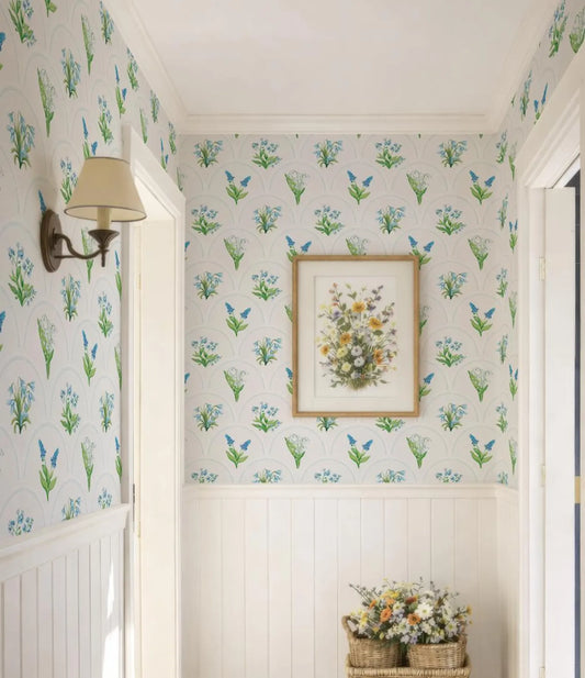 a hallway with a floral wallpaper pattern, a framed picture of flowers on the wall, and a wicker basket filled with flowers on the floor.