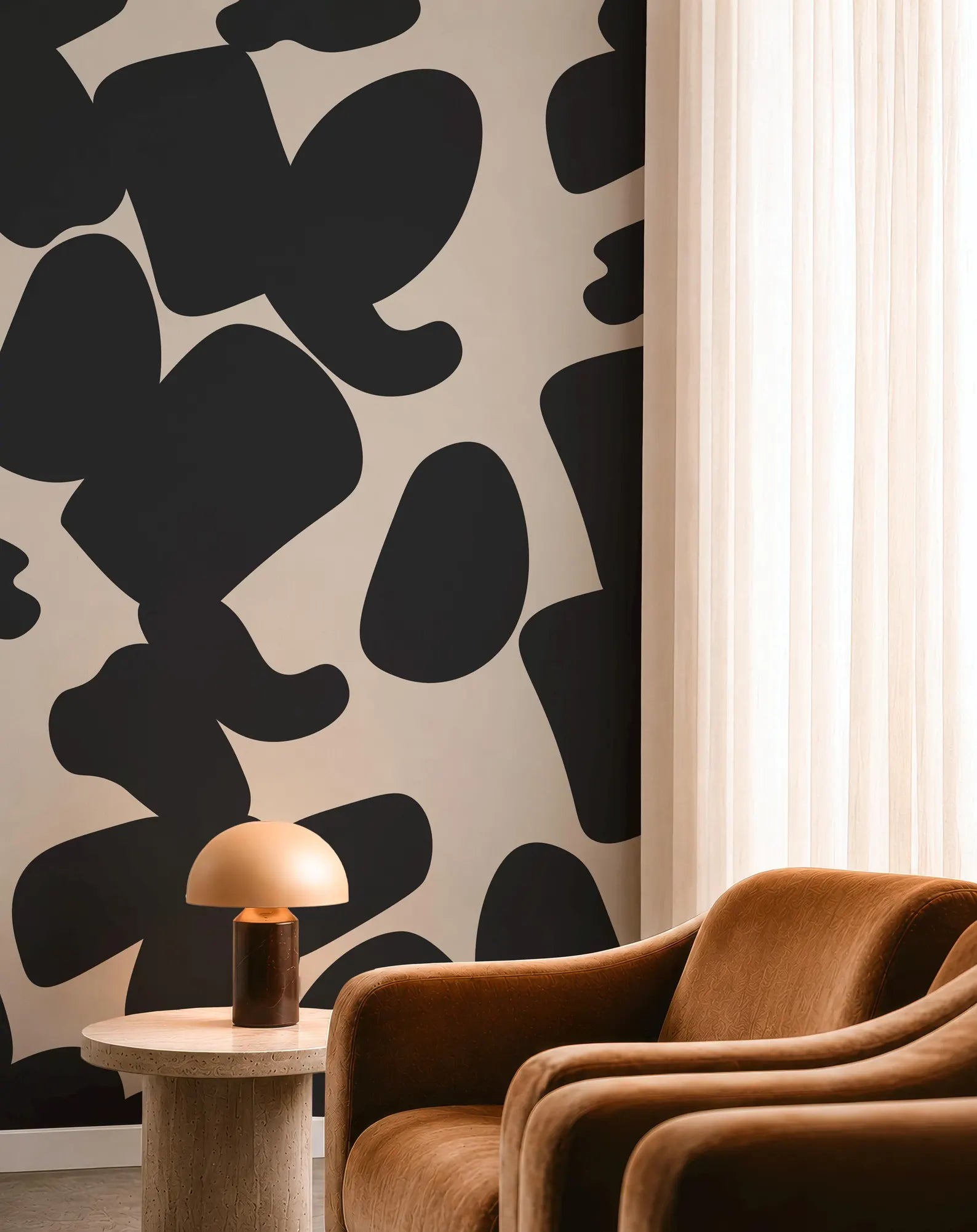 a modern living room with a black and white cow print wallpaper on the wall, a brown armchair, and a small round table with a lamp.