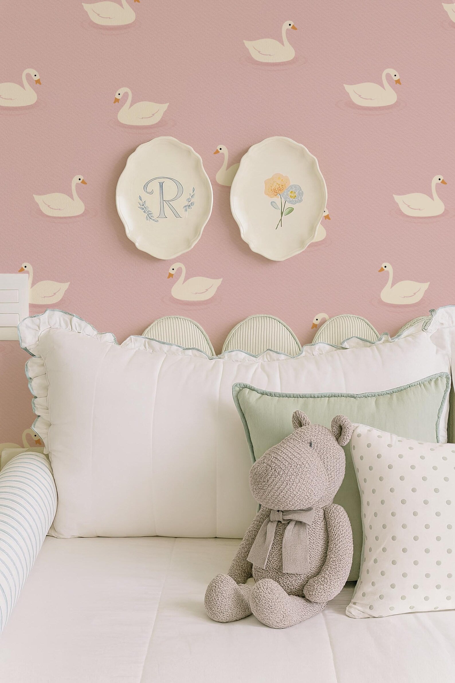 a cozy bedroom scene with a plush stuffed animal, a white bed with decorative pillows, and a wall with a repeating pattern of white swans.
